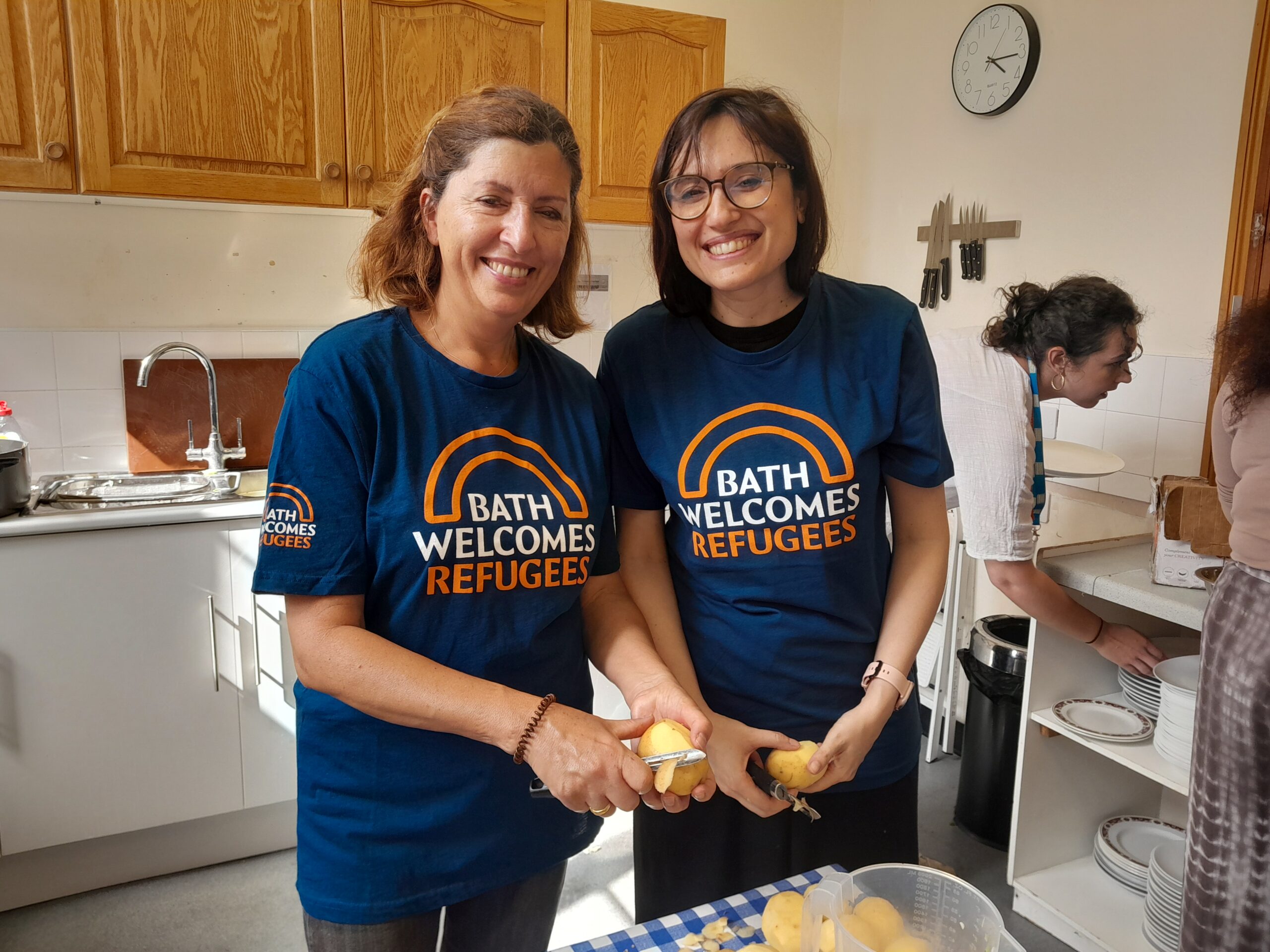 Two women in Bath Welcome Refugees t-shirts helping prepare food